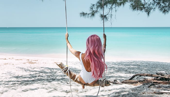 Ragazza con capelli rosa su altalena in spiaggia